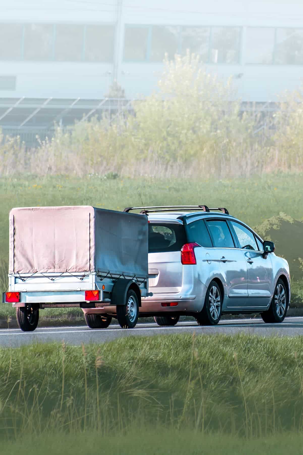 Car towing a small covered utility trailer on a roadway.