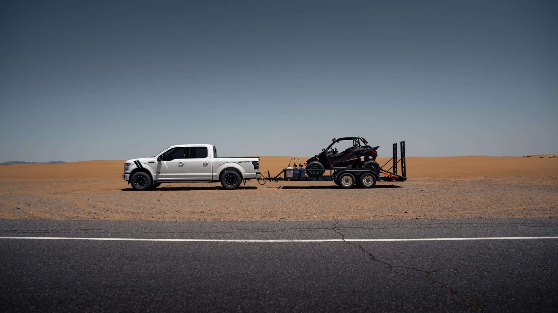 Pickup truck towing an off-road side-by-side on a trailer across a desert highway
