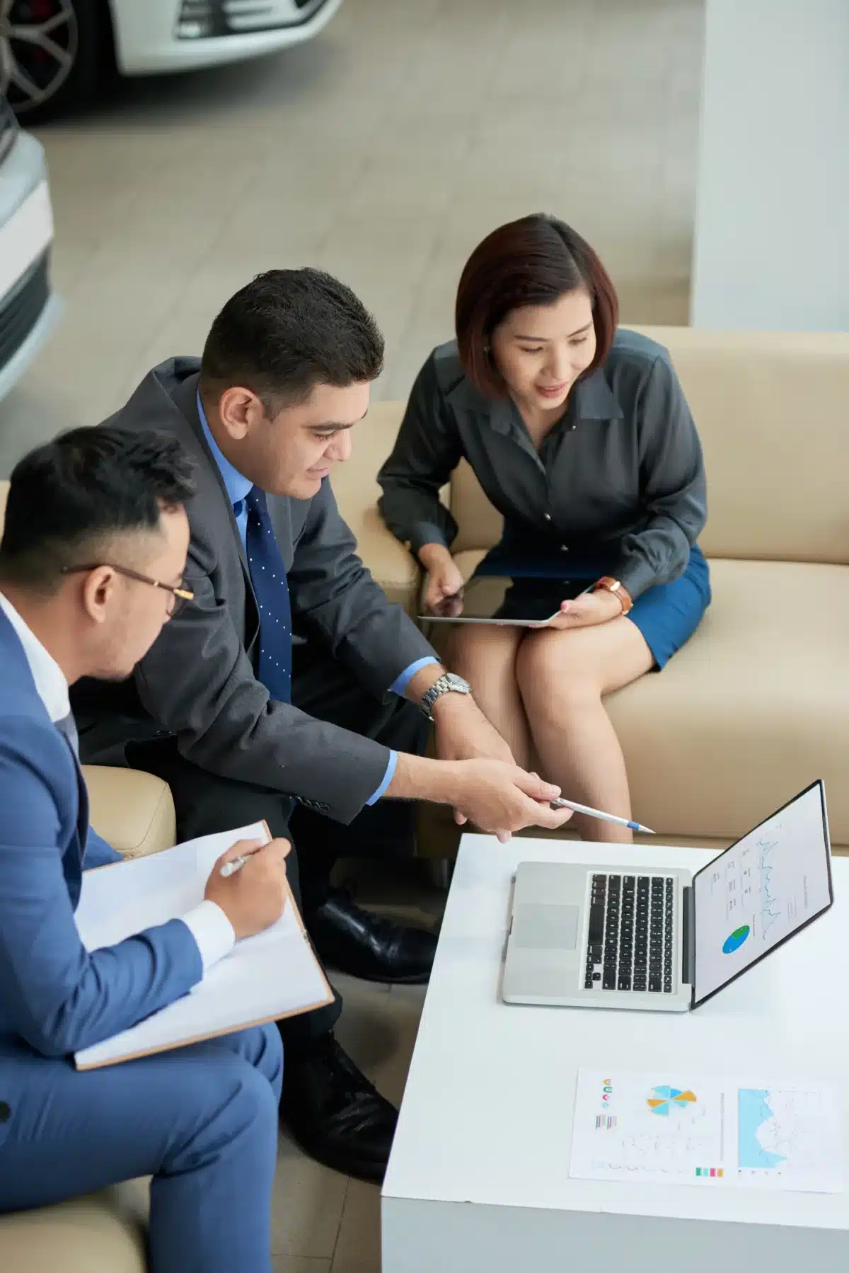 Three professionals discussing graphs on a laptop in a dealership.