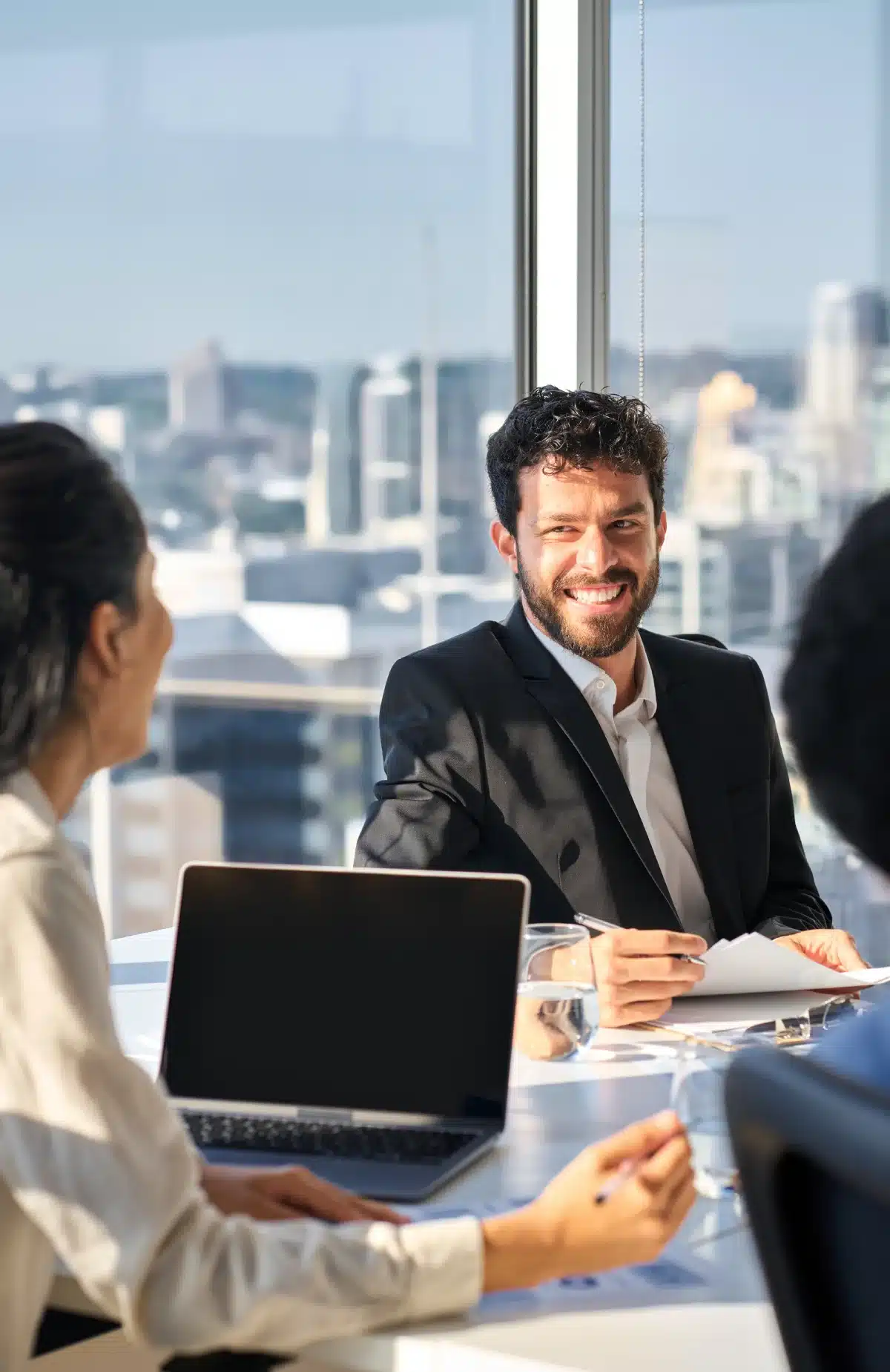 Three people in a meeting with a cityscape view through large windows.